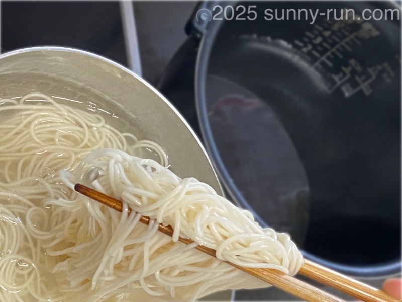 水を入れた炊飯釜に、茹でたそうめんを箸で移して“湯切り”する。