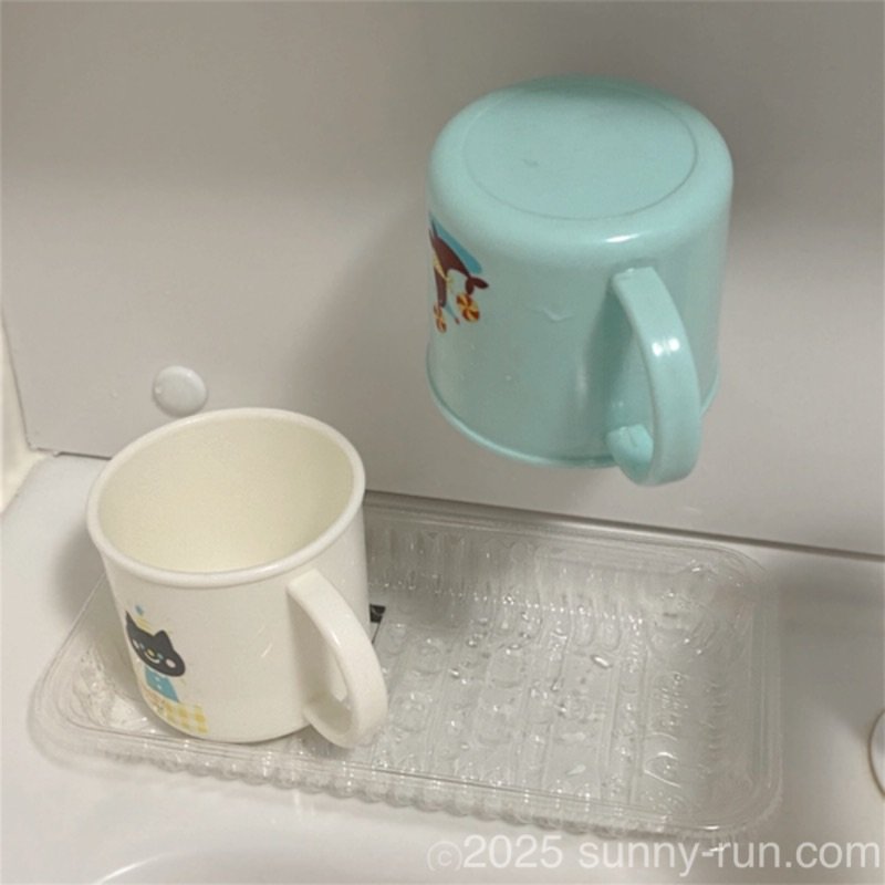 洗面台の「コップ置き」として使っている透明な食品トレーに置いたコップと、コップホルダーにかけたコップ