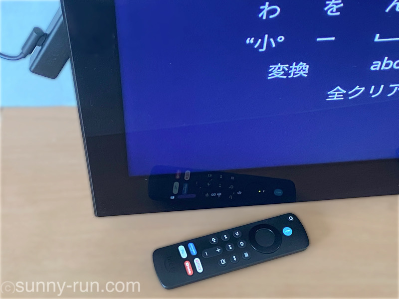 テレビ台に置いたFire TV Stickのリモコンと、テレビ画面に映るプライムビデオの検索画面の一部